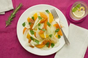 Salade fenouil orange épinard sur nappe magenta avec verre eau citronnée