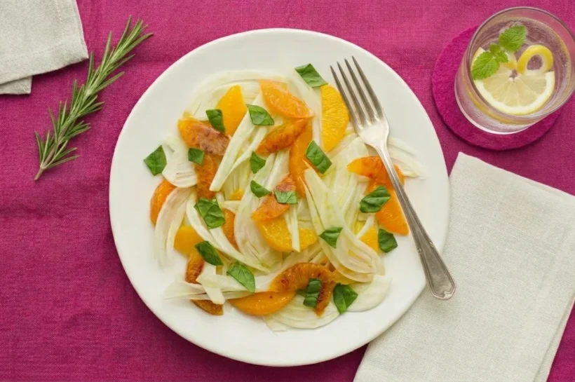 Salade fenouil orange épinard sur nappe magenta avec verre eau citronnée