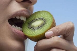 Personne portant une moitié de kiwi près de la bouche.